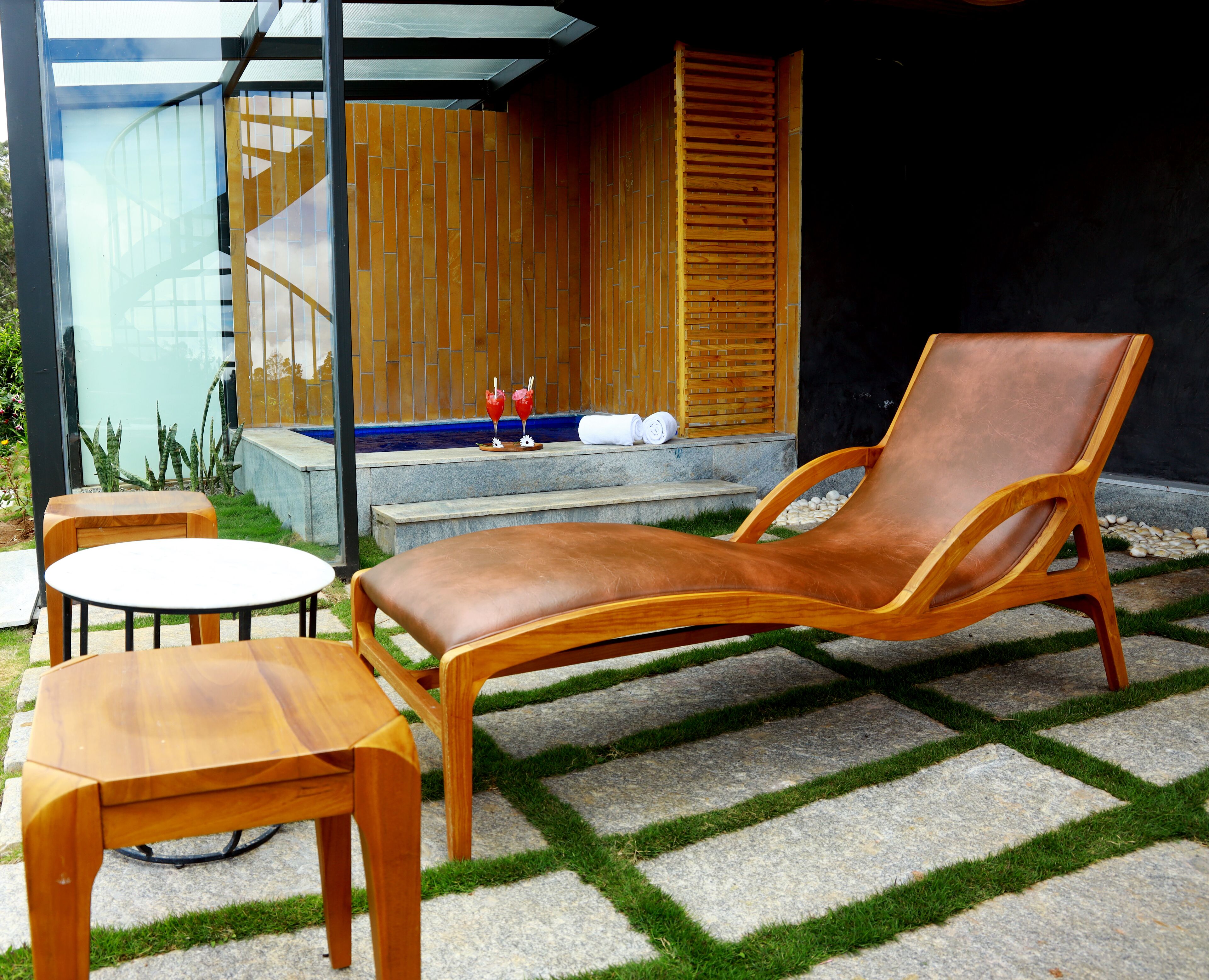 Ein moderner Außenbereich mit Lounge-Möbeln, einem kleinen Tisch, einer Holztreppe und einer Glastür zum Poolbereich.
