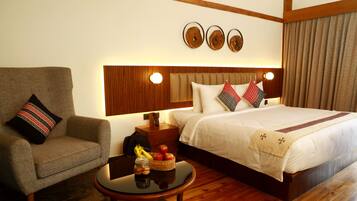 Una habitación de hotel con una cama, una silla, una mesita de noche y una pequeña mesa con fruta y una cesta.