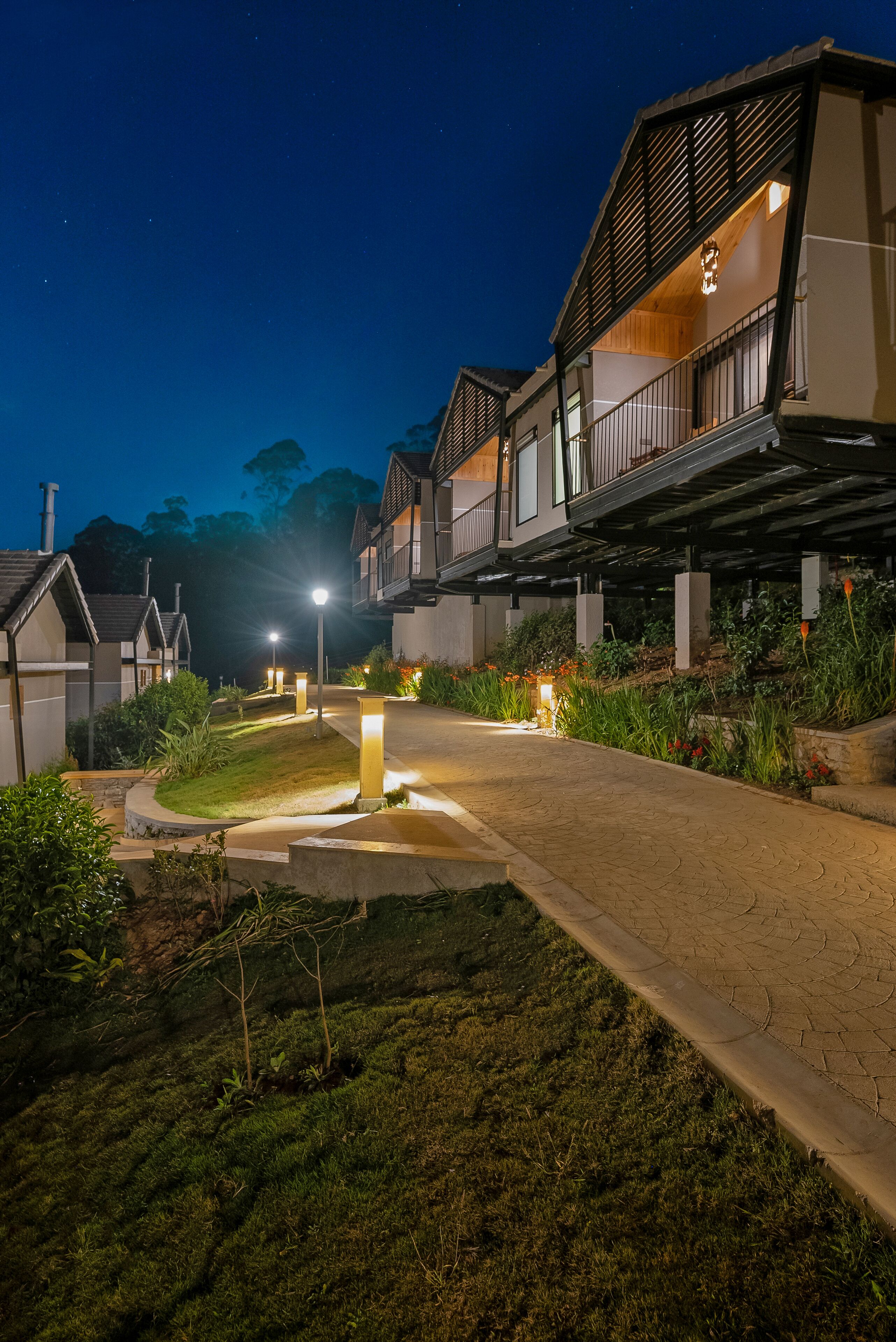 A residential building with a covered walkway, outdoor lighting, and greenery.