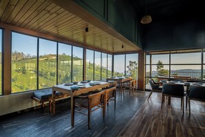 Ruokailutila, jossa on suuret ikkunat, puiset huonekalut ja näkymä vehreille kukkuloille.