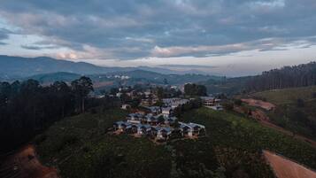 A residential area with multiple houses on a hillside, surrounded by dense forest and rolling hills in the background.