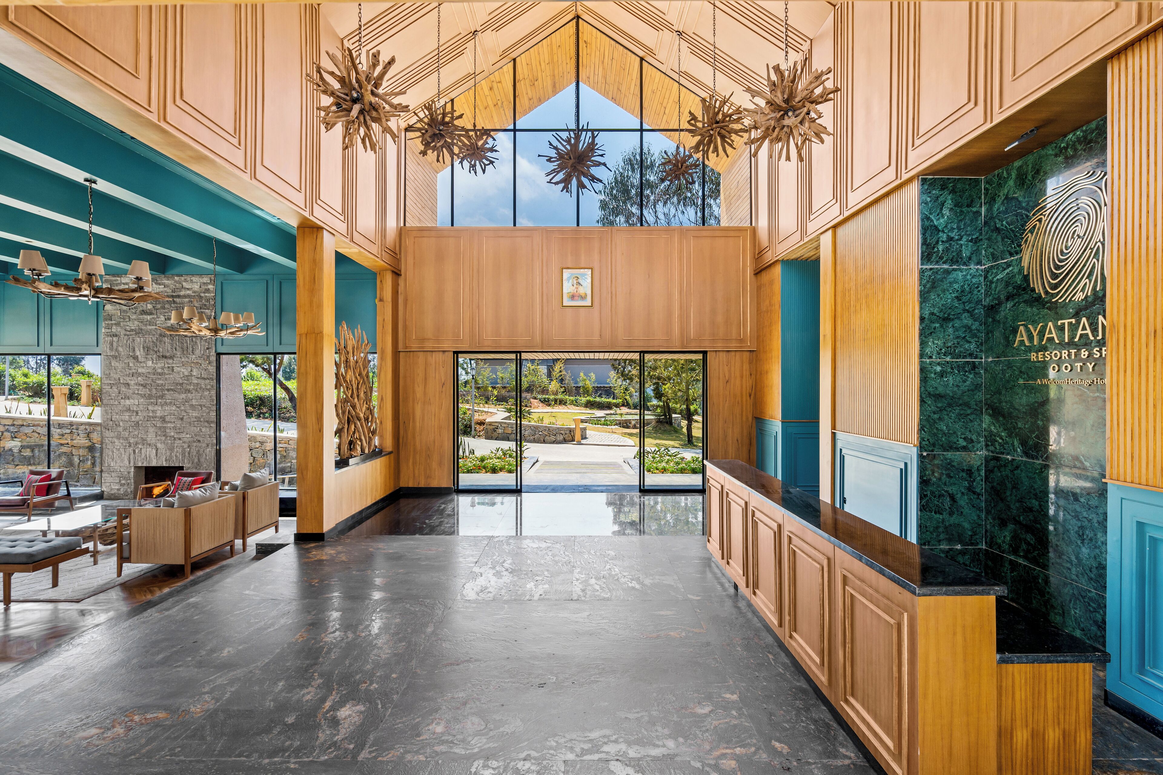 A spacious lobby with a wooden reception desk, a stone fireplace, and a view of the outdoor garden.