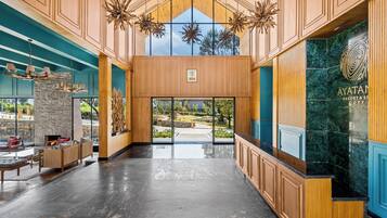 A spacious lobby with a wooden reception desk, a stone fireplace, and a view of the outdoor garden.