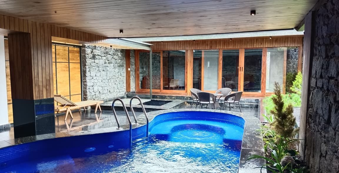 A modern indoor swimming pool with clear water, wooden deck, and lounge chairs.