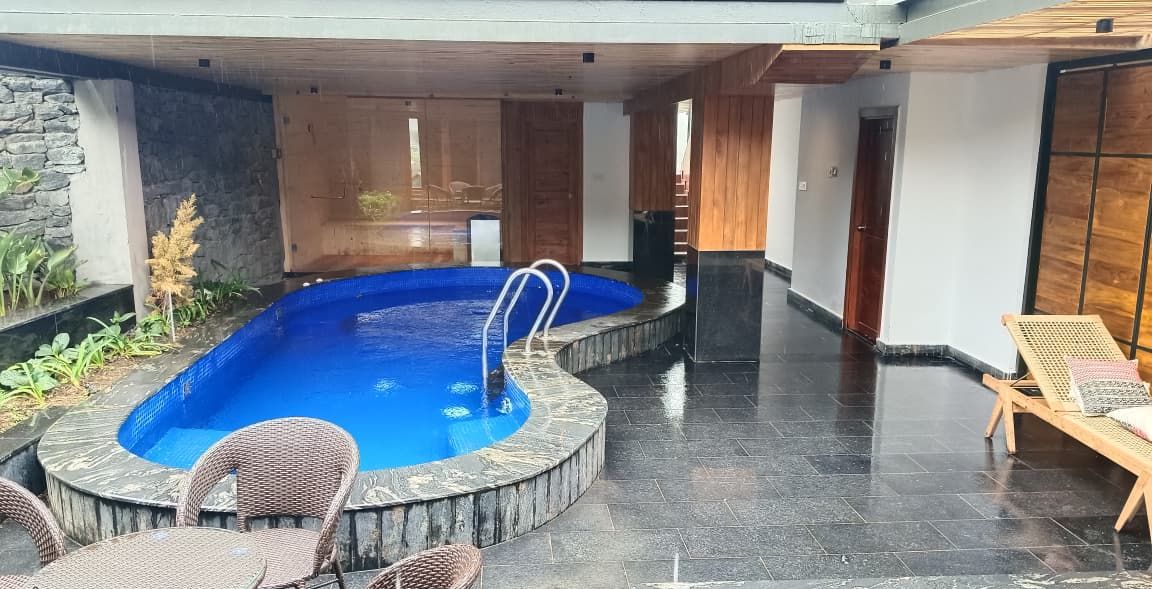 Une piscine entourée d’une terrasse en bois, de fauteuils en osier et d’un espace de détente.
