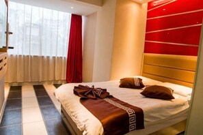 Ein Hotelzimmer mit einem Bett, einem roten Vorhang und einem Fenster mit weißen Jalousien.