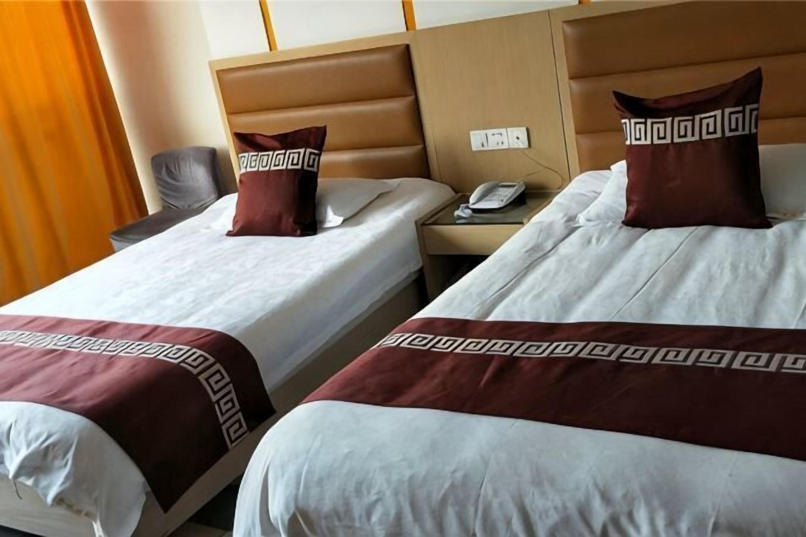 Two adjacent hotel beds with headboards, a bedside table with a phone, and a chair.