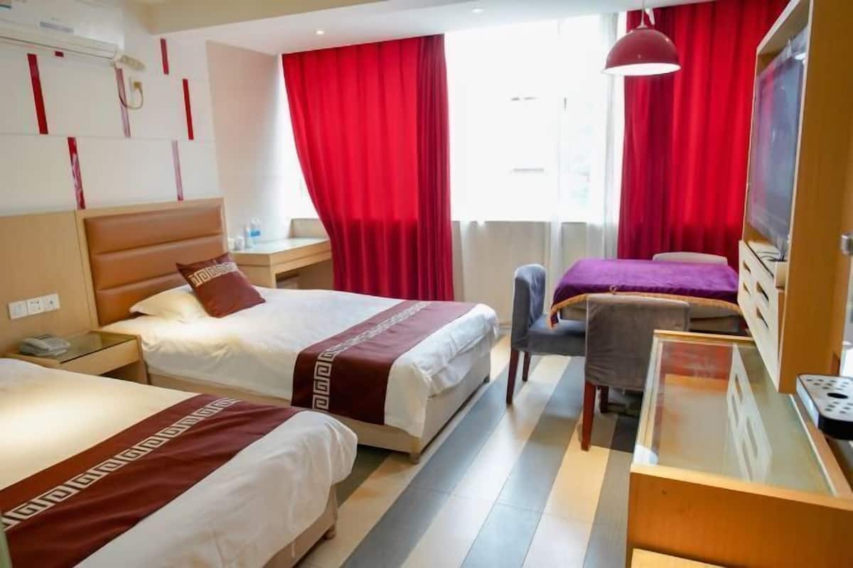 A hotel room with two beds, a desk, a chair, a TV, and red curtains.