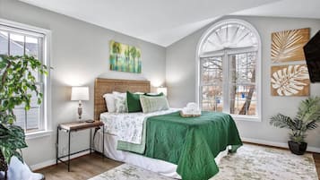Relax in this serene bedroom with a large bed, nightstand, and potted plant, offering a peaceful view of the outdoors through the arched window.