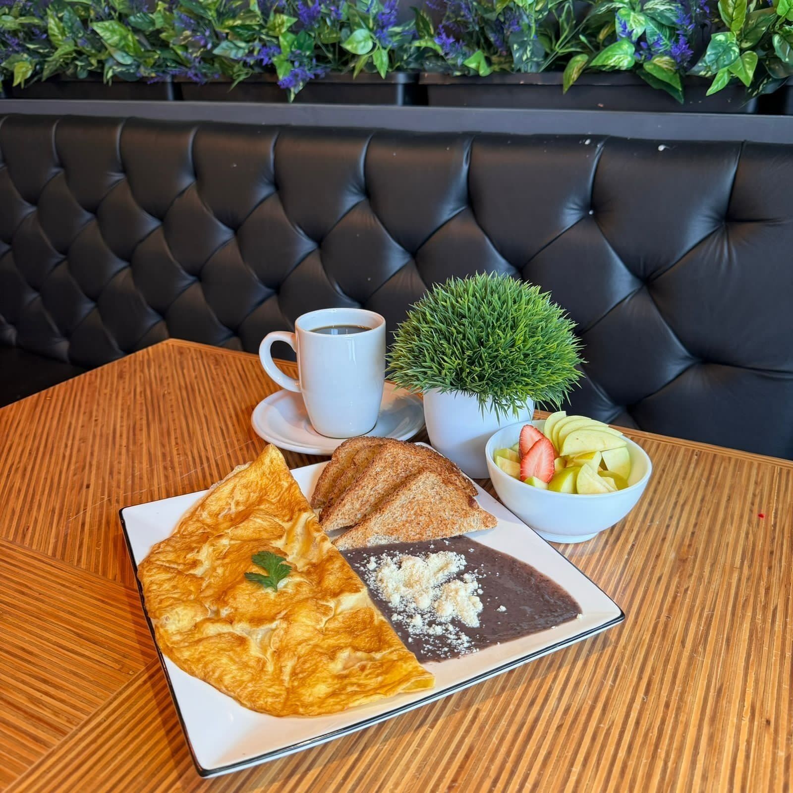 Una mesa con un plato de comida, una taza de café y una pequeña planta.