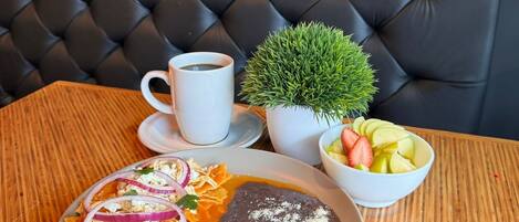 A dining table with a plate of food, a cup of coffee, and a small plant.