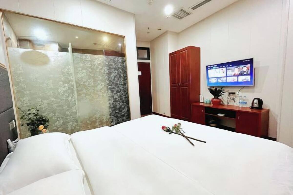 A hotel room with a bed, a TV, a wooden cabinet, and a wall-mounted TV.