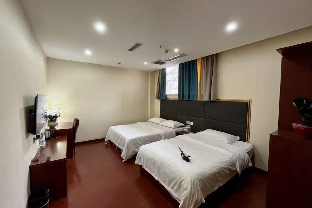 A hotel room with two single beds, a desk with a chair, a television, and a window with curtains.