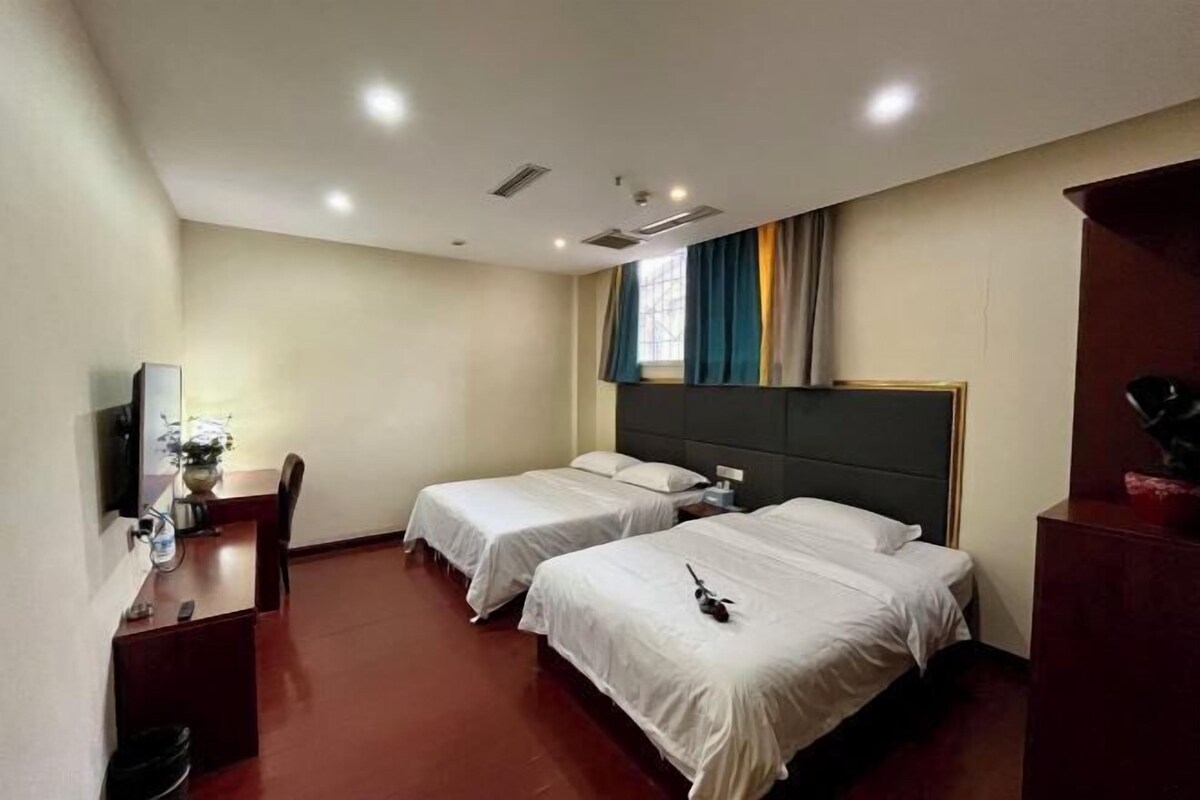 Habitación de hotel con dos camas, un escritorio, una silla, un televisor y una ventana con cortinas.
