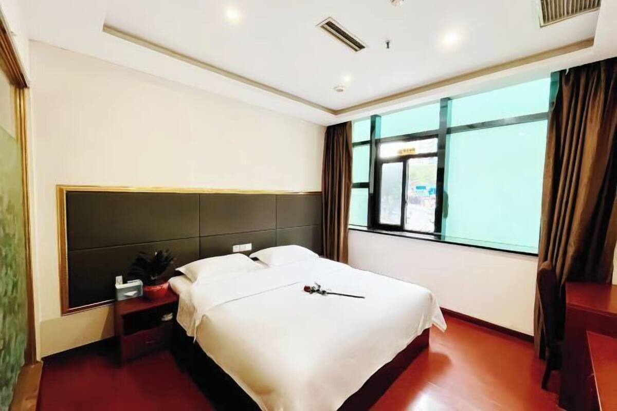 A hotel room with a bed, bedside table, and a window with curtains.