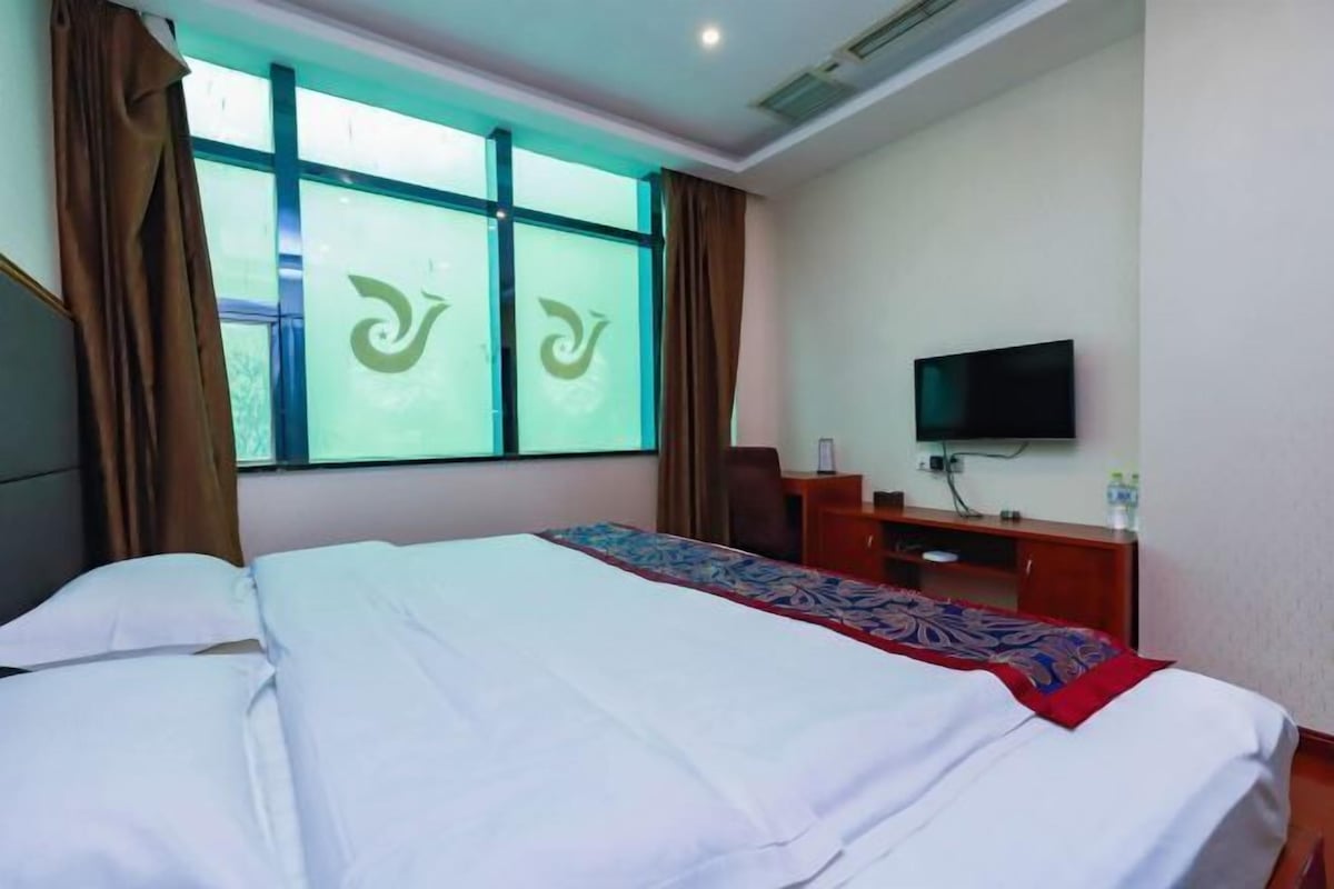 Una habitación de hotel con una cama, televisión, escritorio y ventana con cortinas.