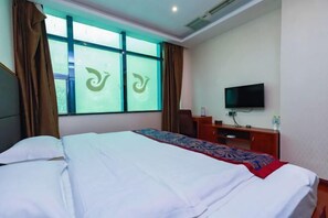 Una habitación de hotel con una cama, televisión, escritorio y ventana con cortinas.