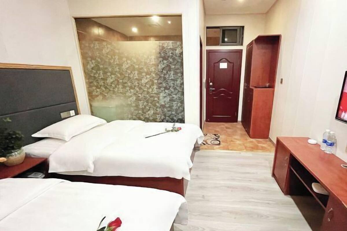 A hotel room with two beds, a desk, a TV, and a shower area.