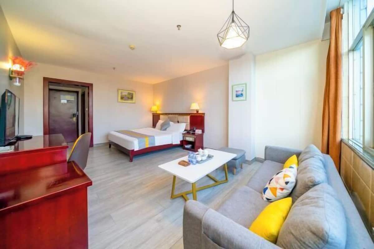 A hotel room with a bed, a sofa, a coffee table, a desk, and a window.