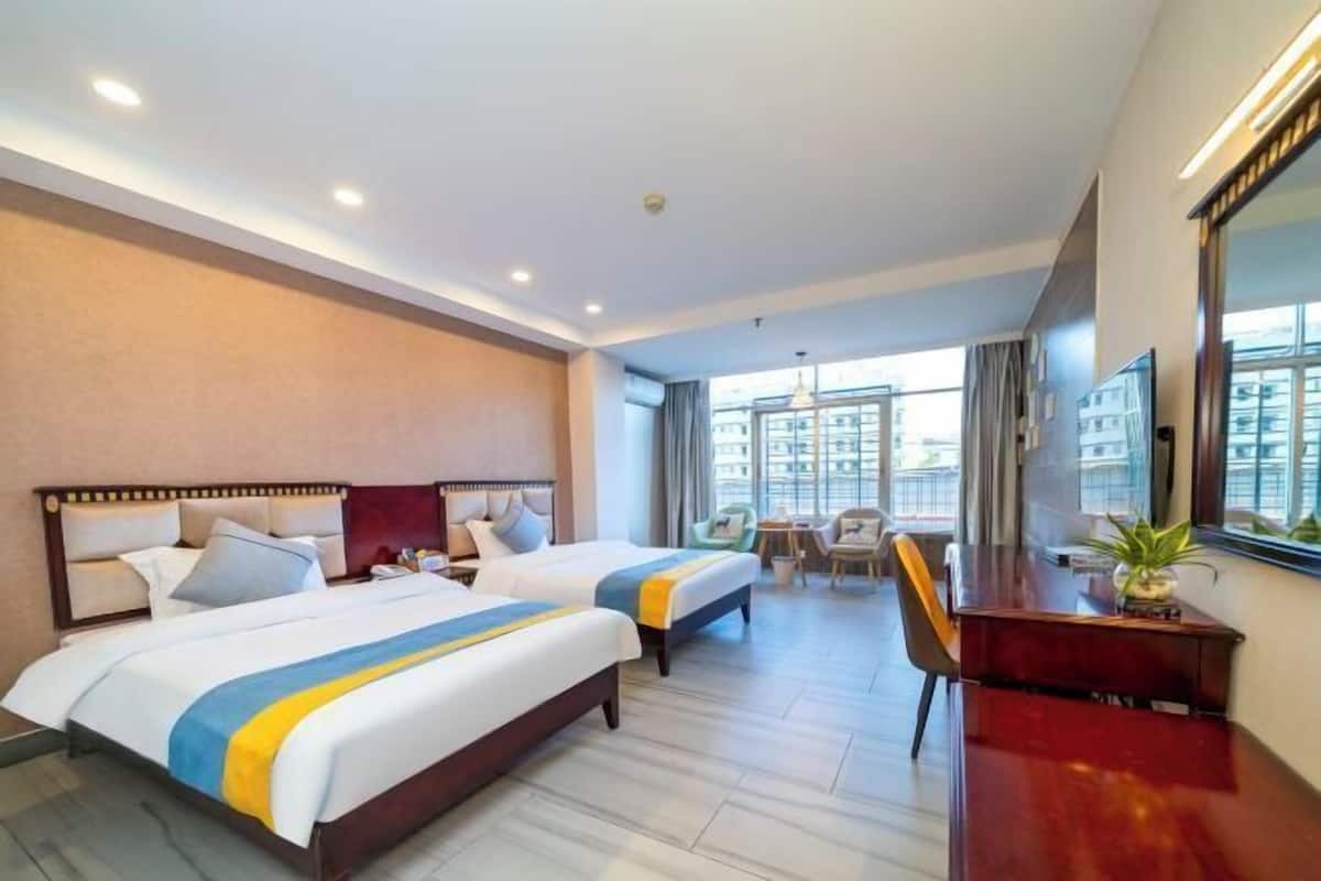 A hotel room with two beds, a desk, a chair, and a large window offering a city view.