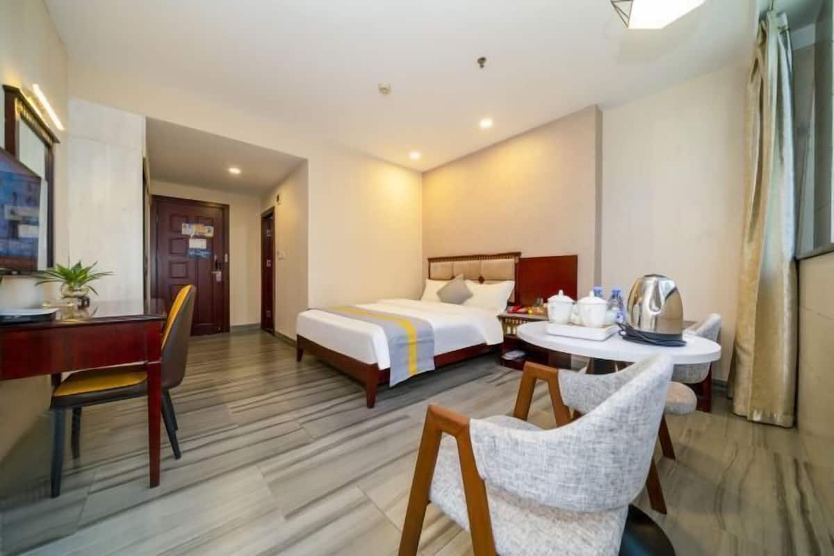 A hotel room with a bed, a desk, a chair, and a dining table.