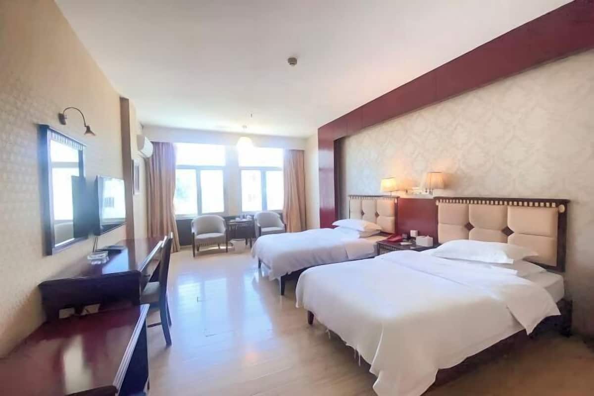 A hotel room with two beds, a desk, a chair, a TV, and a window.