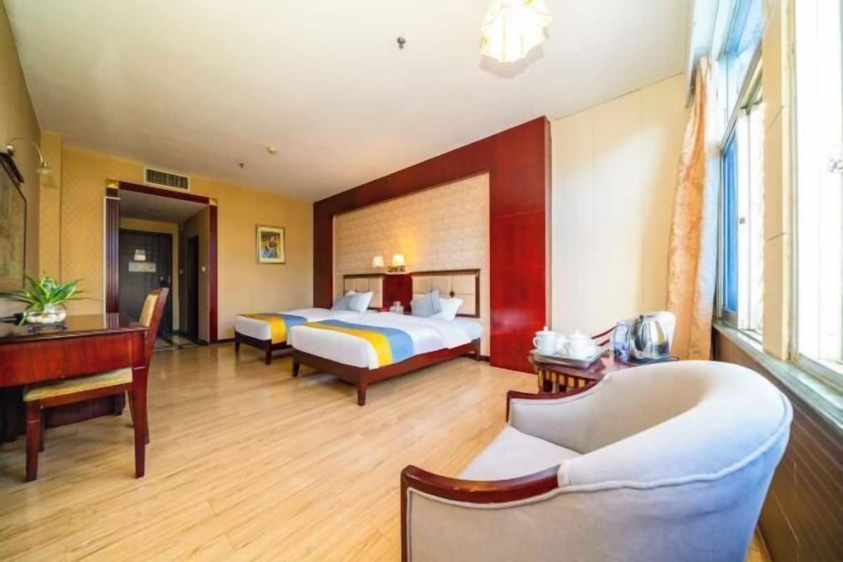 A hotel room with two beds, a desk, a chair, and a window with curtains.
