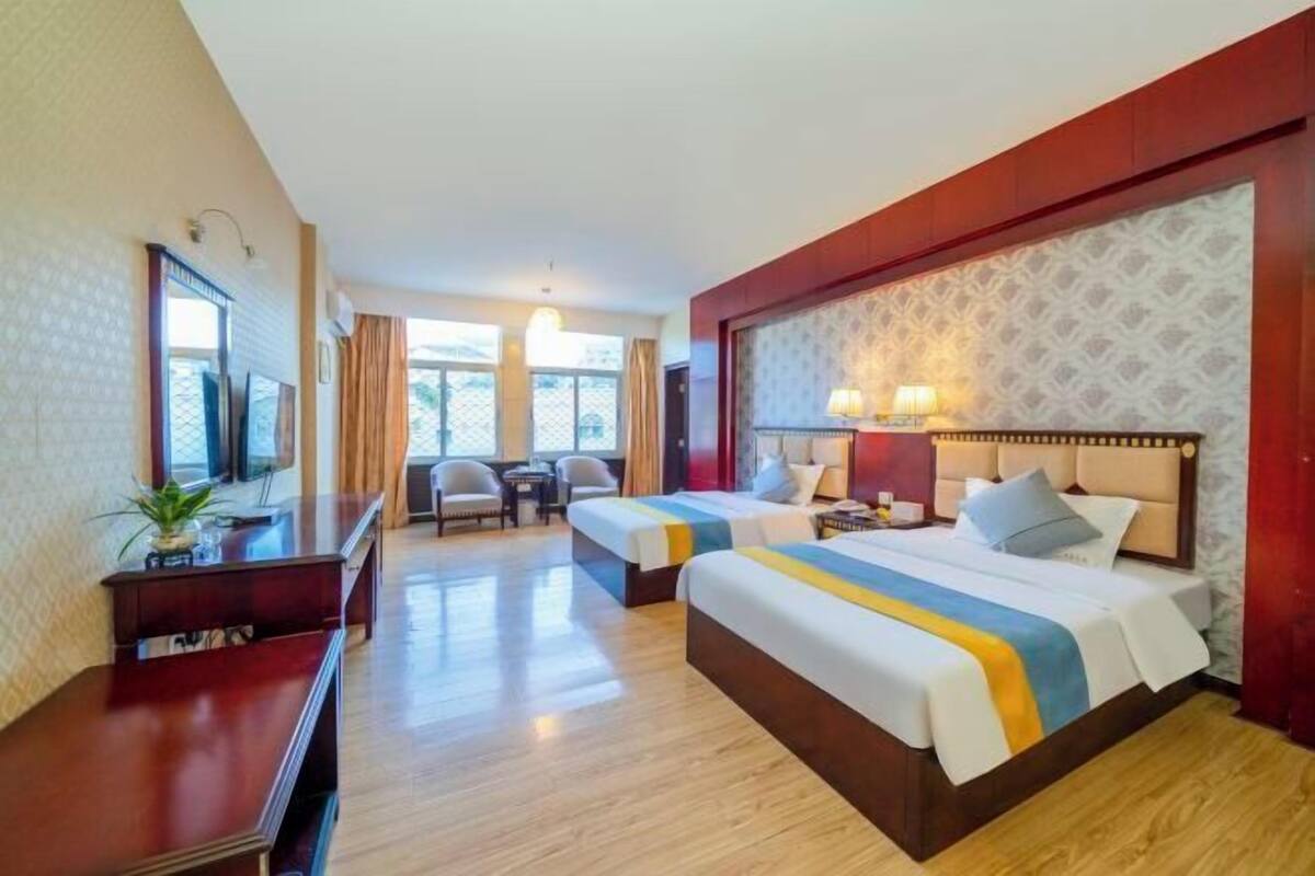 A hotel room with two beds, a desk, a TV, and a window with curtains.