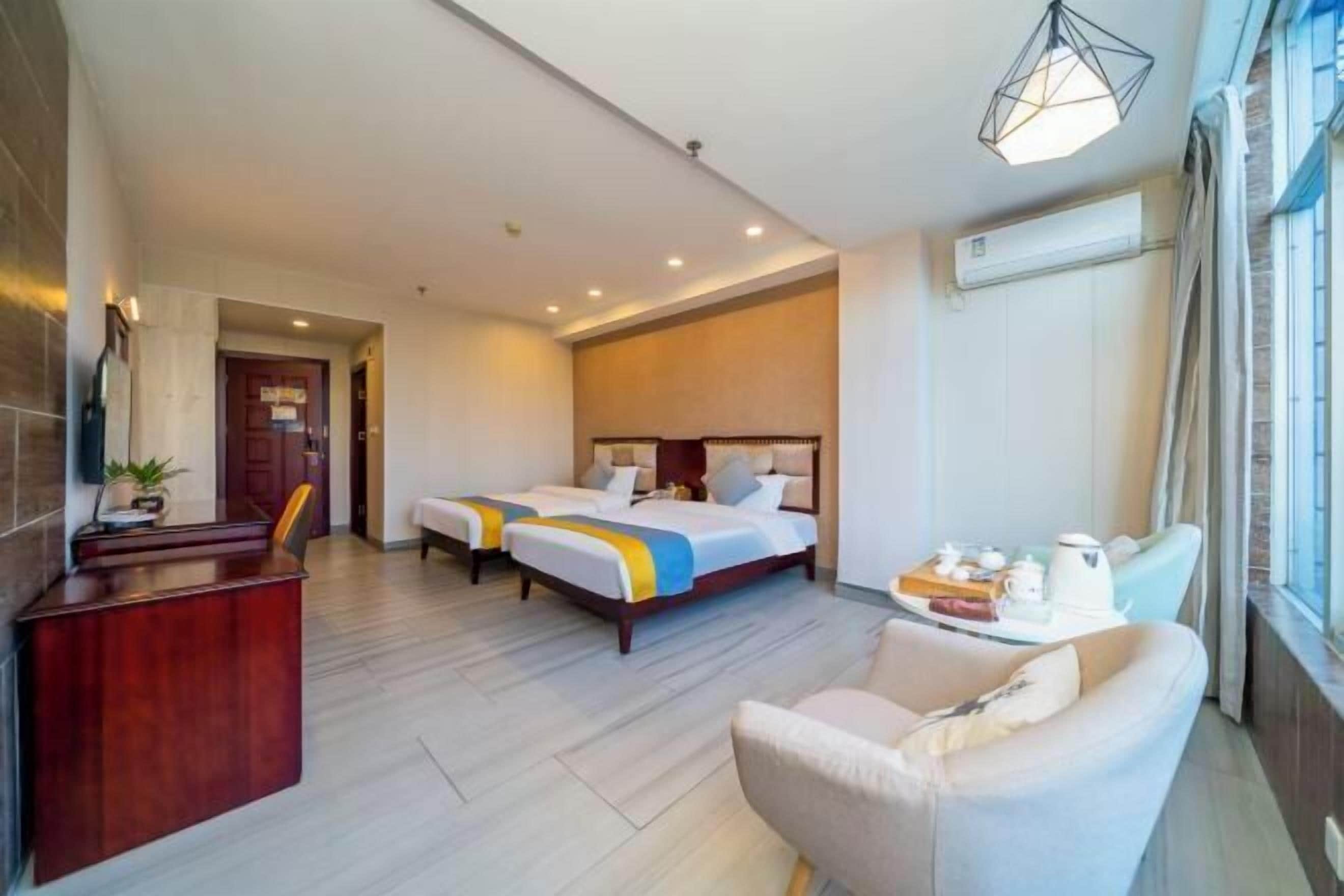 A hotel room with two beds, a desk, a chair, and a window with curtains.