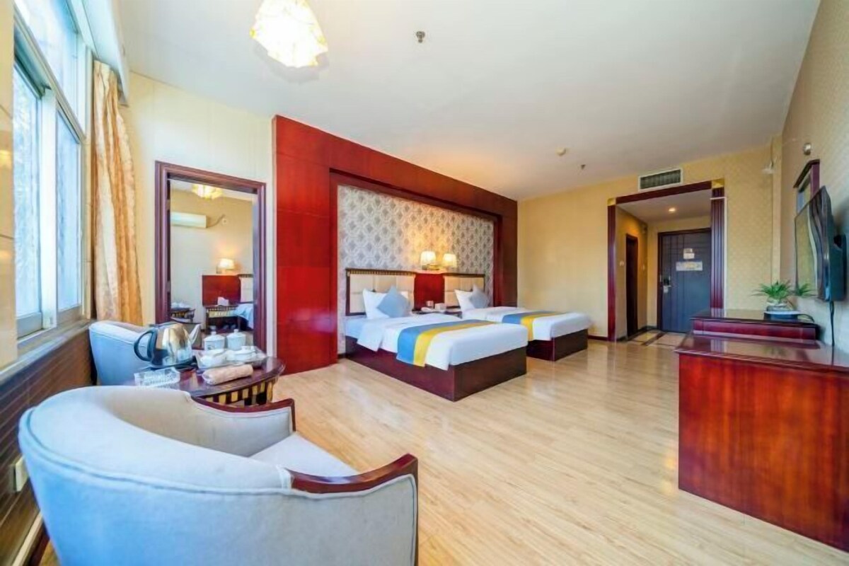 Quarto de hotel com duas camas, uma escrivaninha, uma cadeira, um espelho e uma televisão.