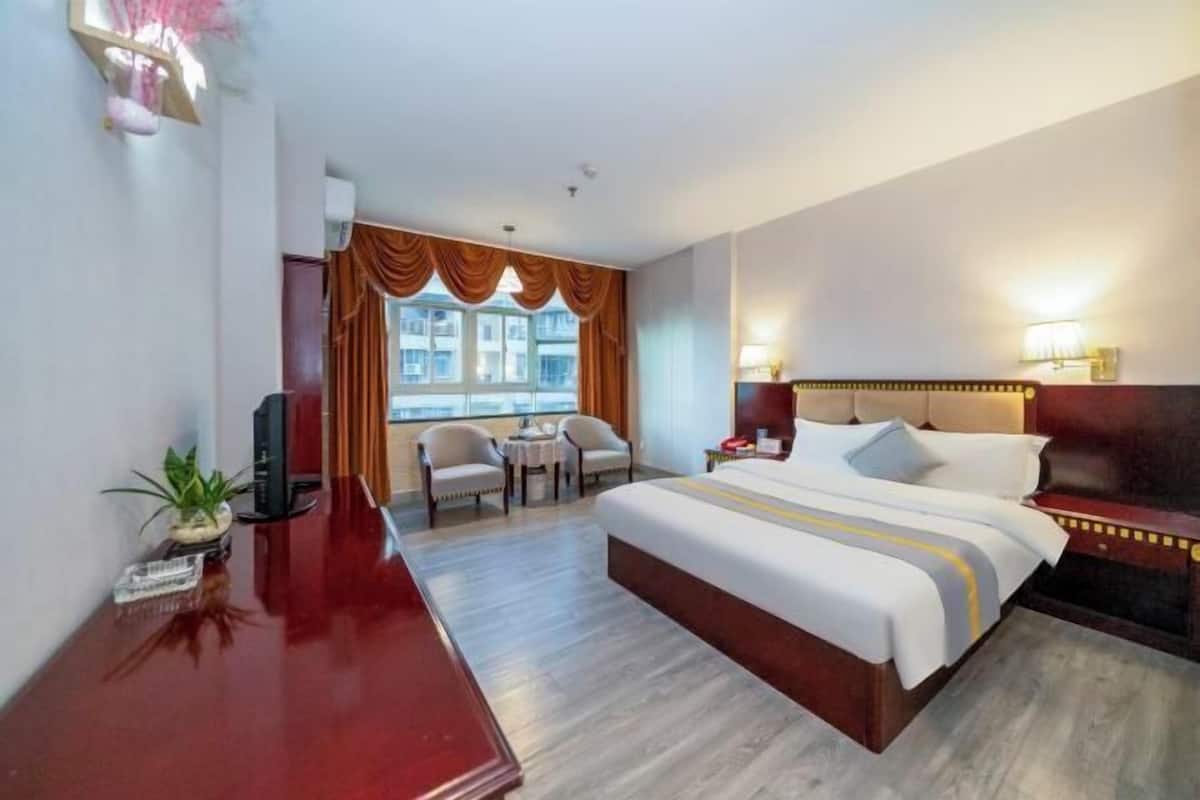 A hotel room with a large bed, a desk, a chair, a small table, and a window with curtains.