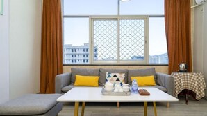 A modern living room with a grey sofa, yellow cushions, a white coffee table, and a window with a view of buildings. - Nan'an Furong Hotel (Guoguang High School Meishan Bus Station) (Nan'an)