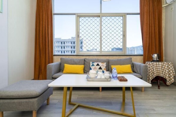 Ein modernes Wohnzimmer mit einem grauen Sofa, gelben Kissen, einem weißen Couchtisch und einem Fenster mit Blick auf Gebäude.
