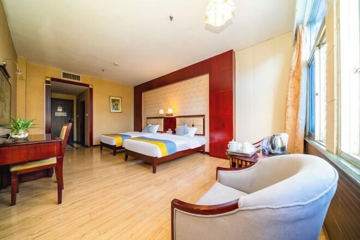 Quarto de hotel com duas camas, uma escrivaninha, uma cadeira e uma janela.