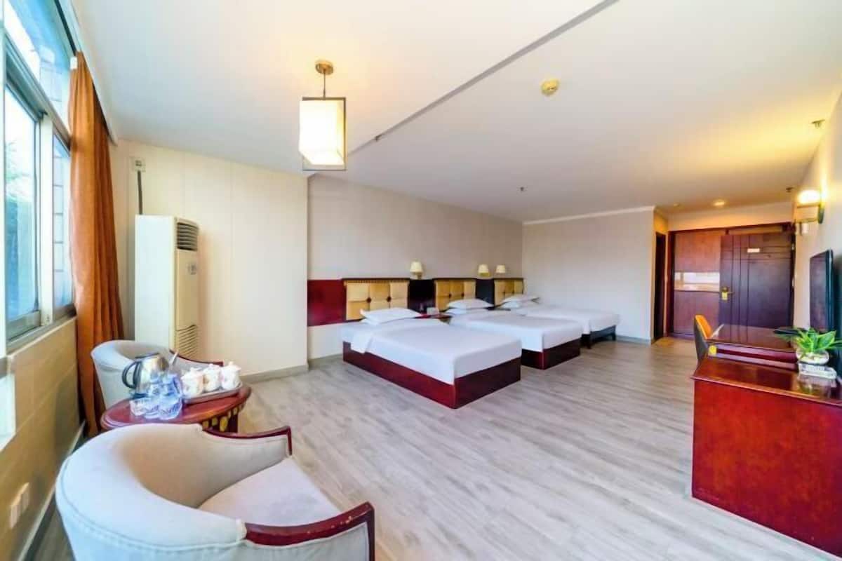 A hotel room with two beds, a desk, a chair, a TV, and a window.