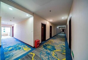 Ein Hotelkorridor mit Teppichboden mit floralem Muster, Türen auf beiden Seiten und einem roten Mülleimer.