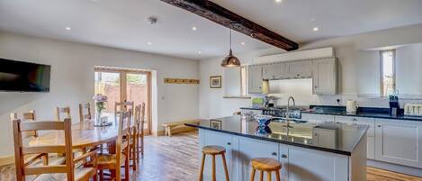 A spacious kitchen with a central island, wooden dining table, and bar stools.