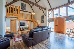 A spacious living area with a large leather sofa, wooden staircase, and a television. - Bristow's Barn | East Ruston Cottages. East Ruston, Norfolk (East Ruston)