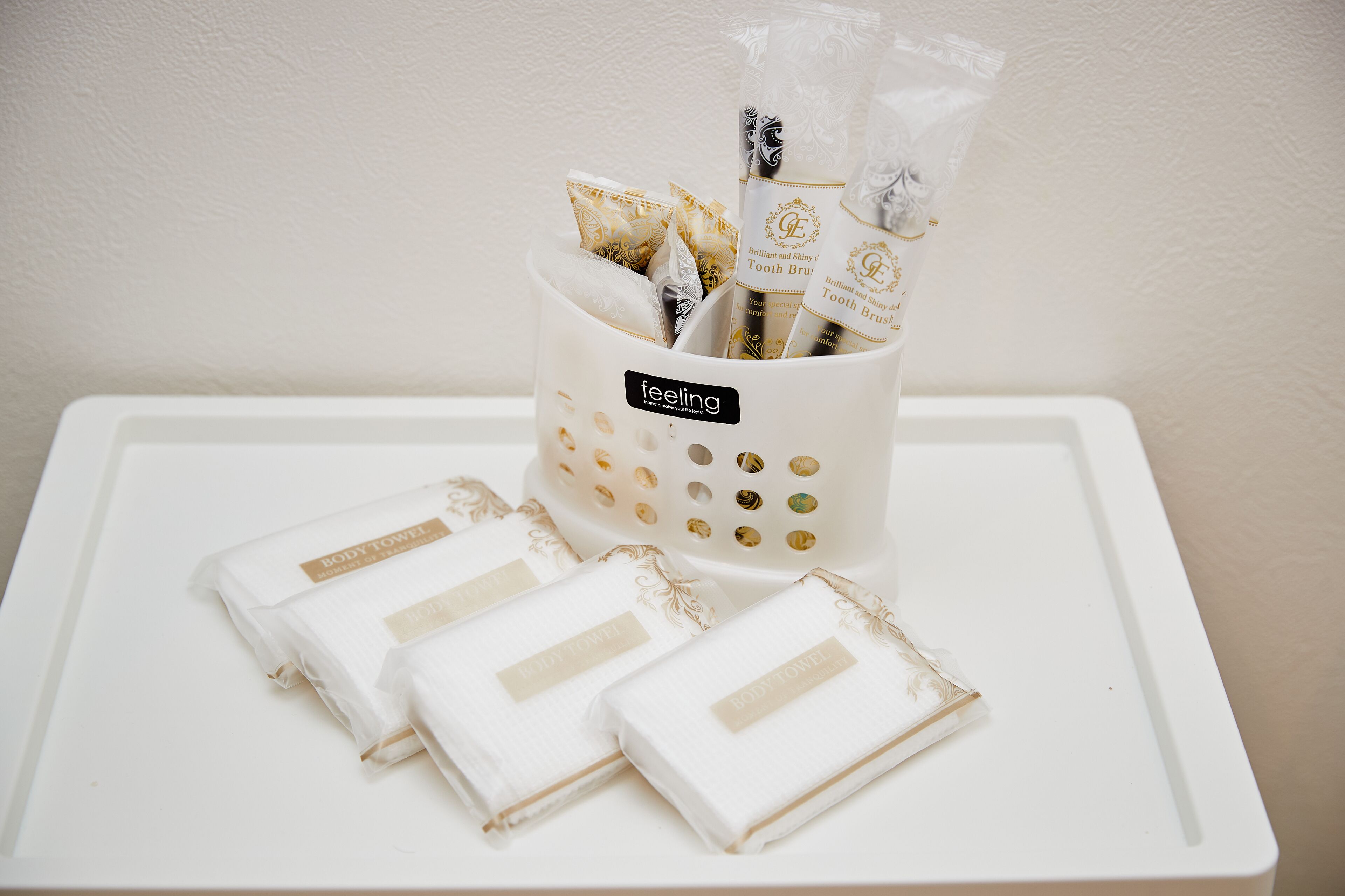 A white tray with a white cup containing toothpastes and a white towel with a label.
