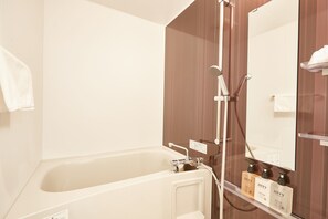 A bathroom with a bathtub, a shower, and a mirror. There are toiletries on the counter.