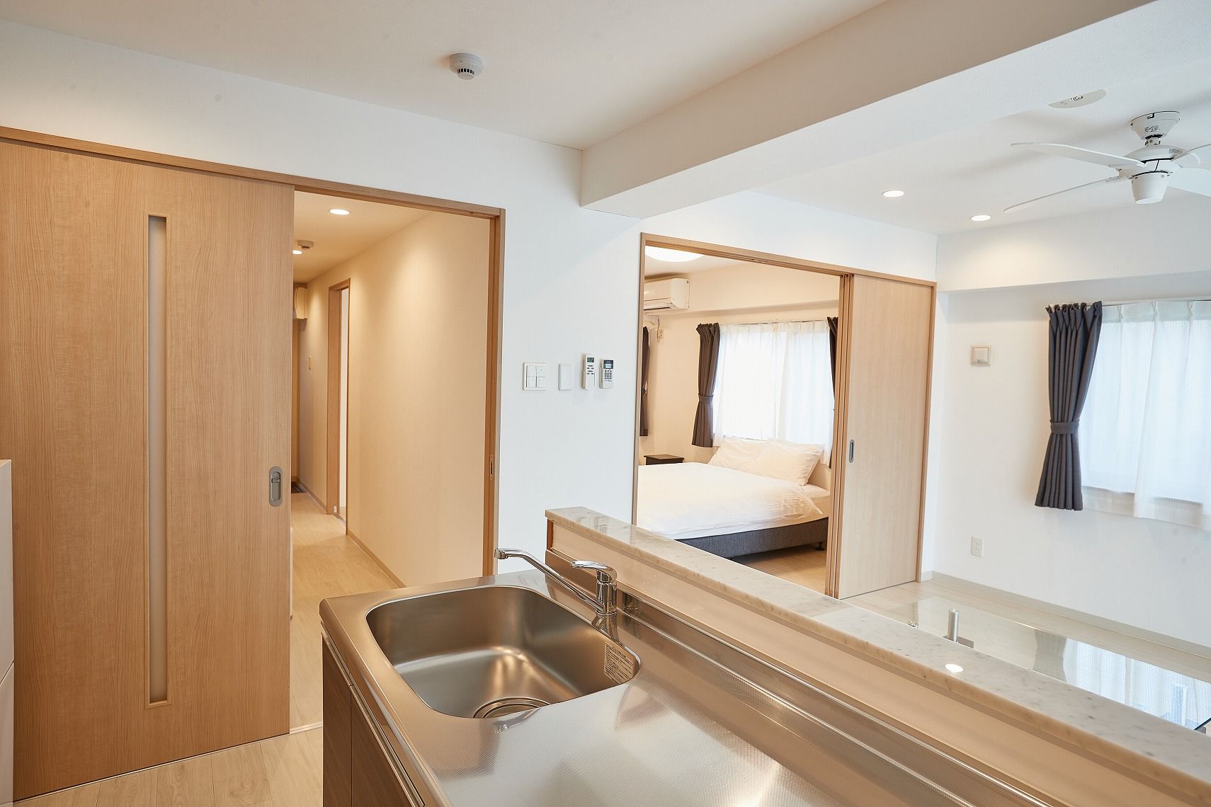A hotel room with a wooden door, a sink, a bed, a ceiling fan, and a window with curtains.