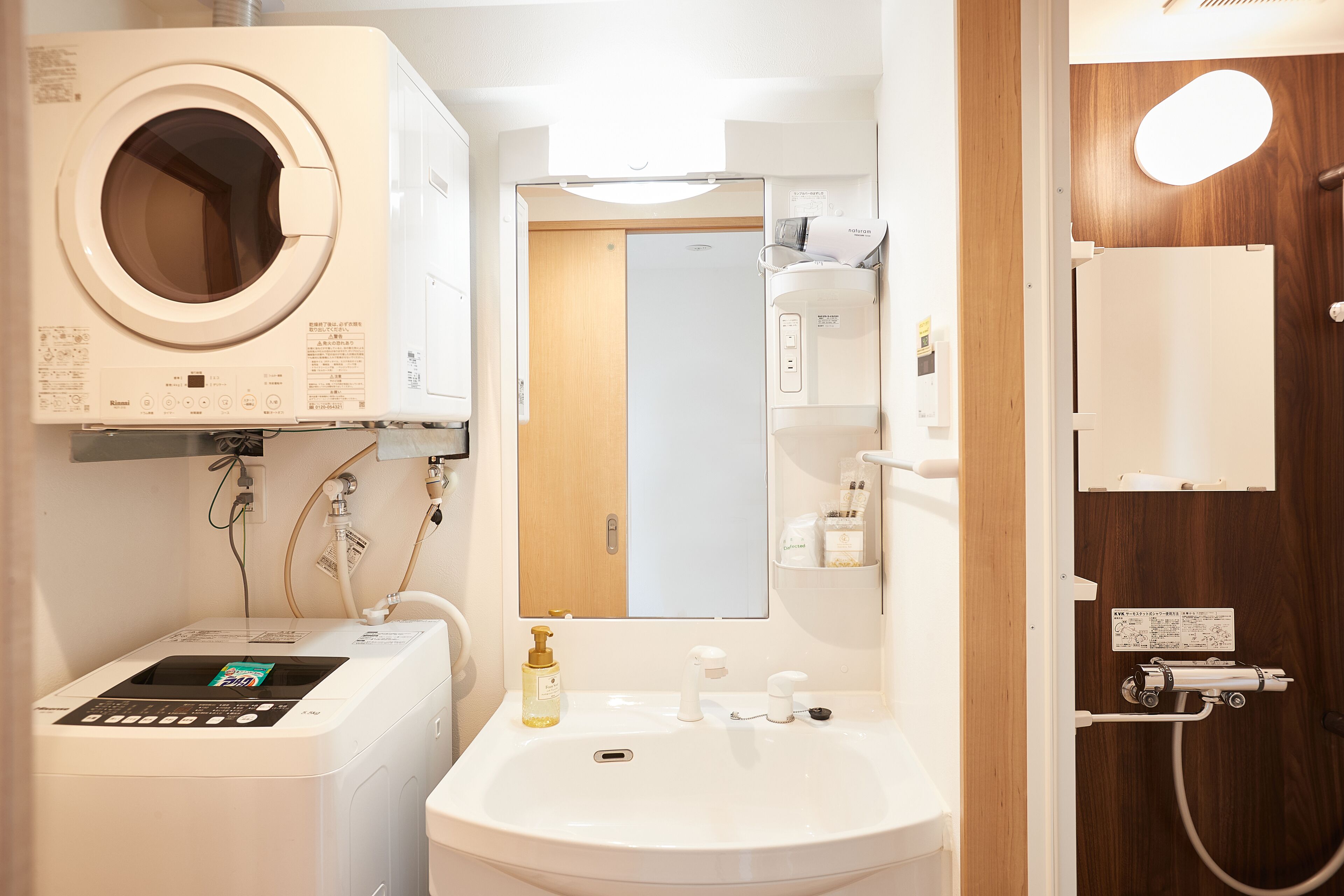 A compact bathroom with a washing machine, a sink, and a shower area.