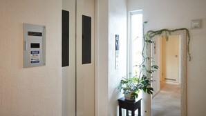 A hallway with a door, a potted plant, and a wall-mounted device. - New Normal Hotel in NAGO (Nago)