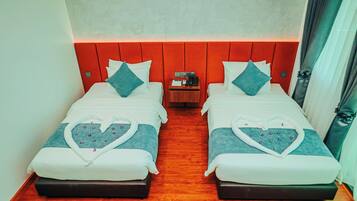 Habitación de hotel con dos camas, cada una con toallas con forma de corazón, suelo de madera y una mesita de noche con un teléfono y una lámpara.