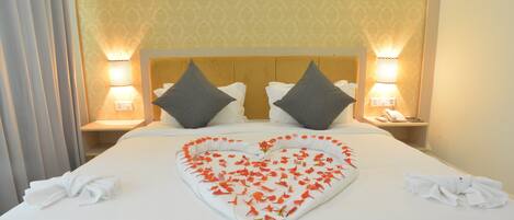 Habitación de hotel con una cama grande, dos almohadas, lámparas de noche y una decoración con forma de corazón en la cama.