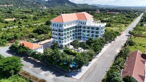 A multi-story hotel with a red roof, surrounded by lush greenery and a clear road.