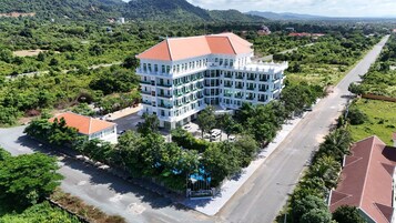 Un hotel de varios pisos con techo rojo, rodeado de exuberante vegetación y una carretera despejada.