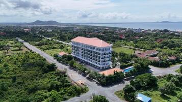 A multi-story hotel with a red roof, surrounded by greenery and a view of the sea.