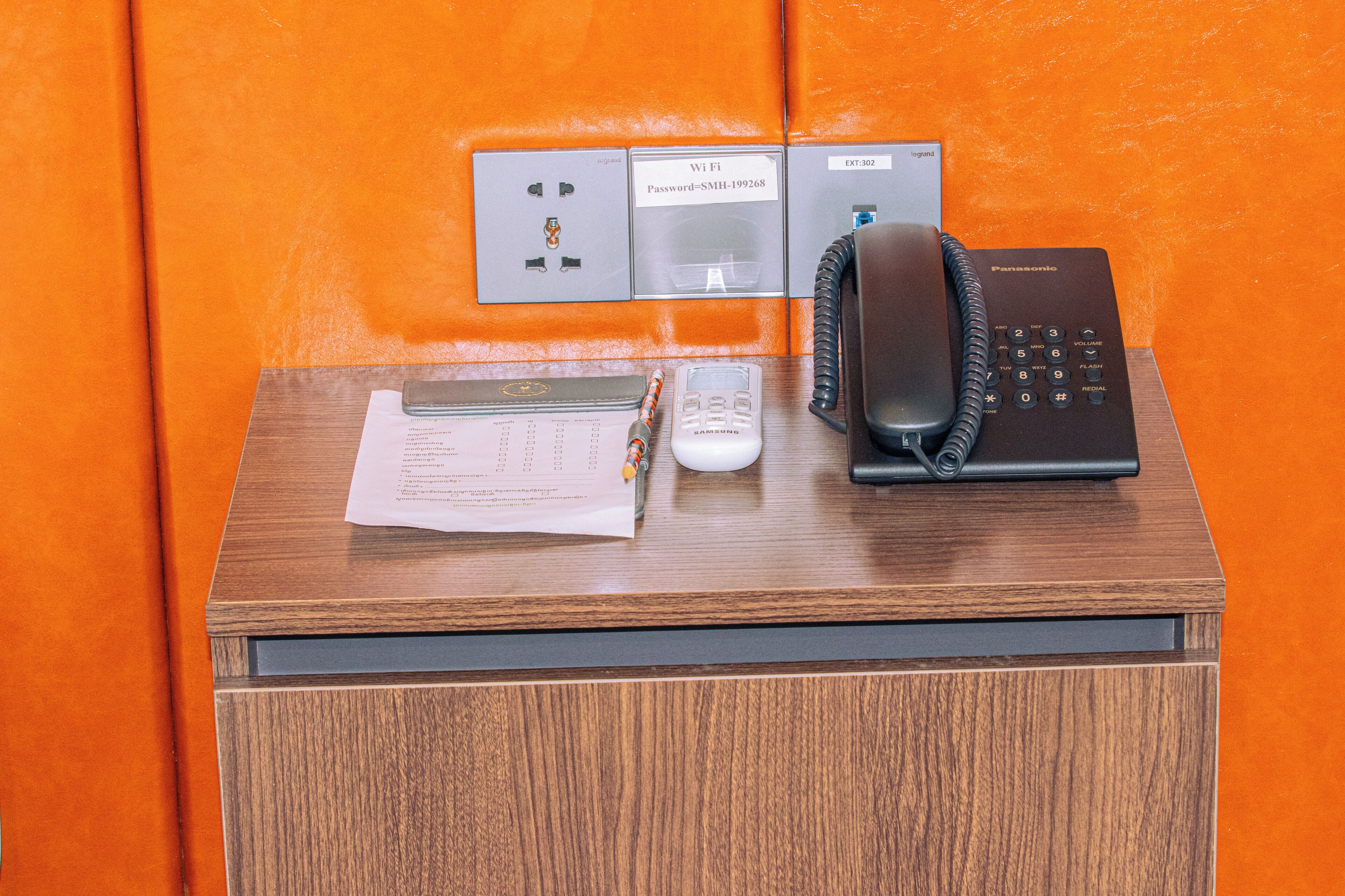 Un bureau en bois avec un téléphone Panasonic, un appareil blanc et des papiers.
