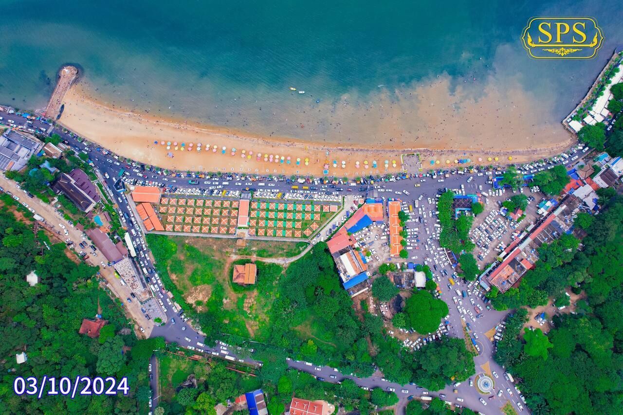 An aerial view of a coastal area with a beach, parking lots, and buildings.